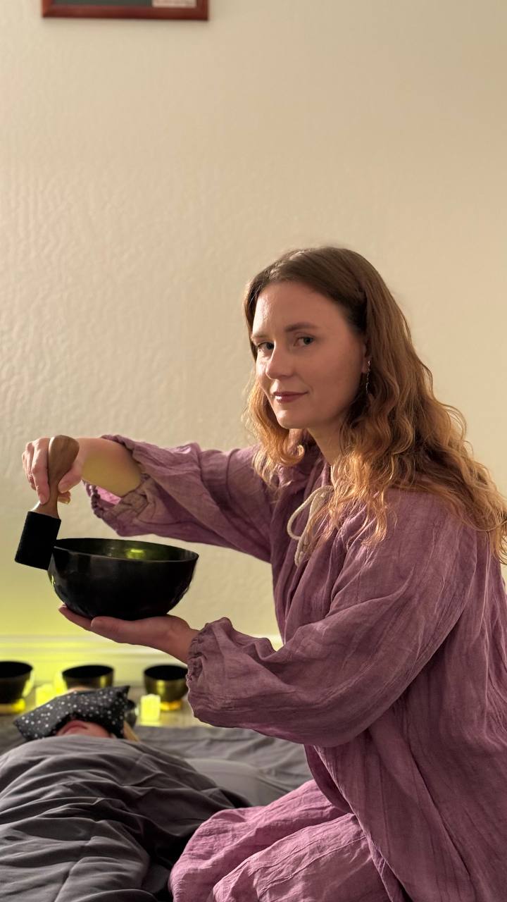 Anastasia playing a Tibetan bowl during a session while a client rests with an eye mask